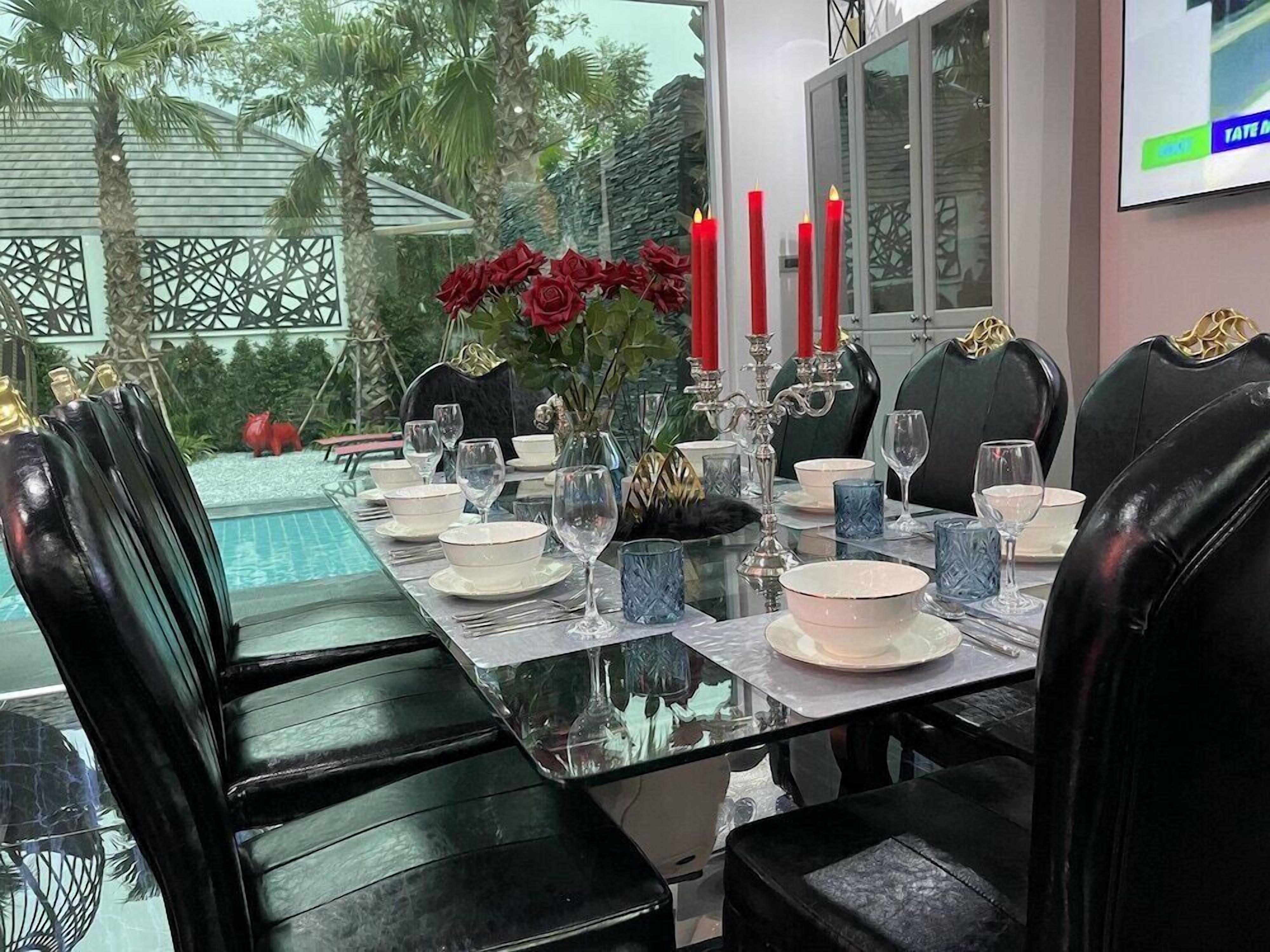 Une table à manger dressée pour six personnes, avec des chaises en cuir noir, des bougies rouges et un vase rempli de fleurs rouges.