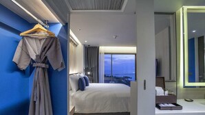 A modern hotel room with a large bed, a robe hanging on the wall, and a view of the city at dusk. - Vip Villas Pattaya Hollywood Jomtien Beach (Pattaya)