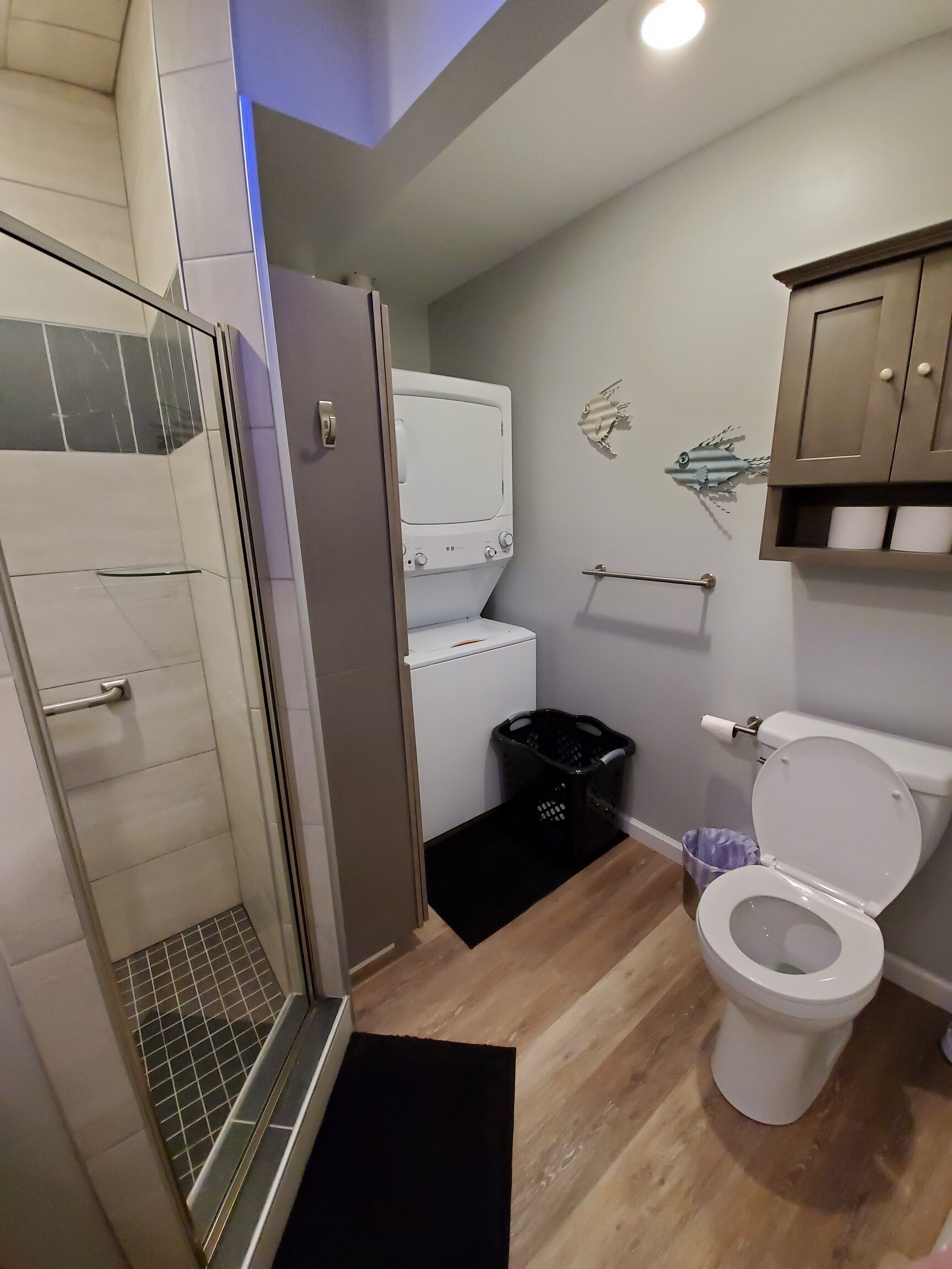 Ein modernes Badezimmer mit bodengleicher Dusche, Toilette und integriertem Waschmaschinenanschluss.