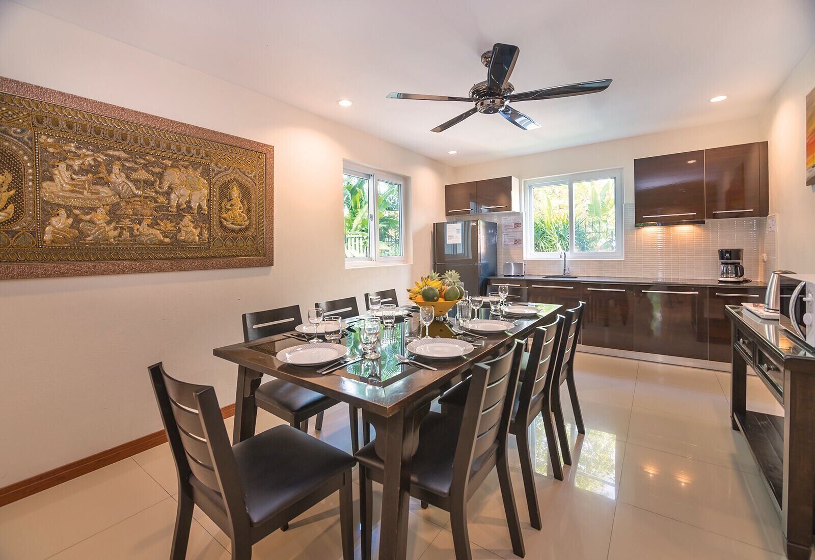 A modern kitchen with dark cabinetry, a central island, and a dining area with a glass table set for six.