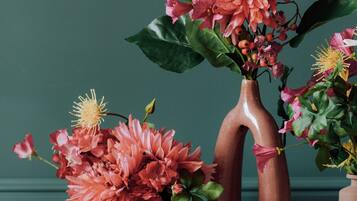 Three ceramic vases with flowers on a wooden surface against a teal wall.