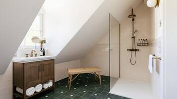 A bathroom with a wooden vanity, a bench, a shower, and a tiled floor.