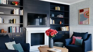 A modern living room with dark blue sofas, a fireplace, a bookshelf, and a flat-screen TV. - Villa Alma - a lakeside Boutique Hotel (St. Gilgen)