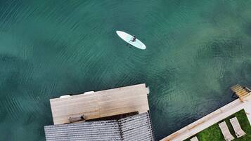 An aerial view of a swimming area with a surfboard, a wooden deck, and a poolside lounge area.