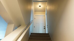 Un escalier menant à une porte blanche, au-dessus de laquelle se trouve un luminaire.