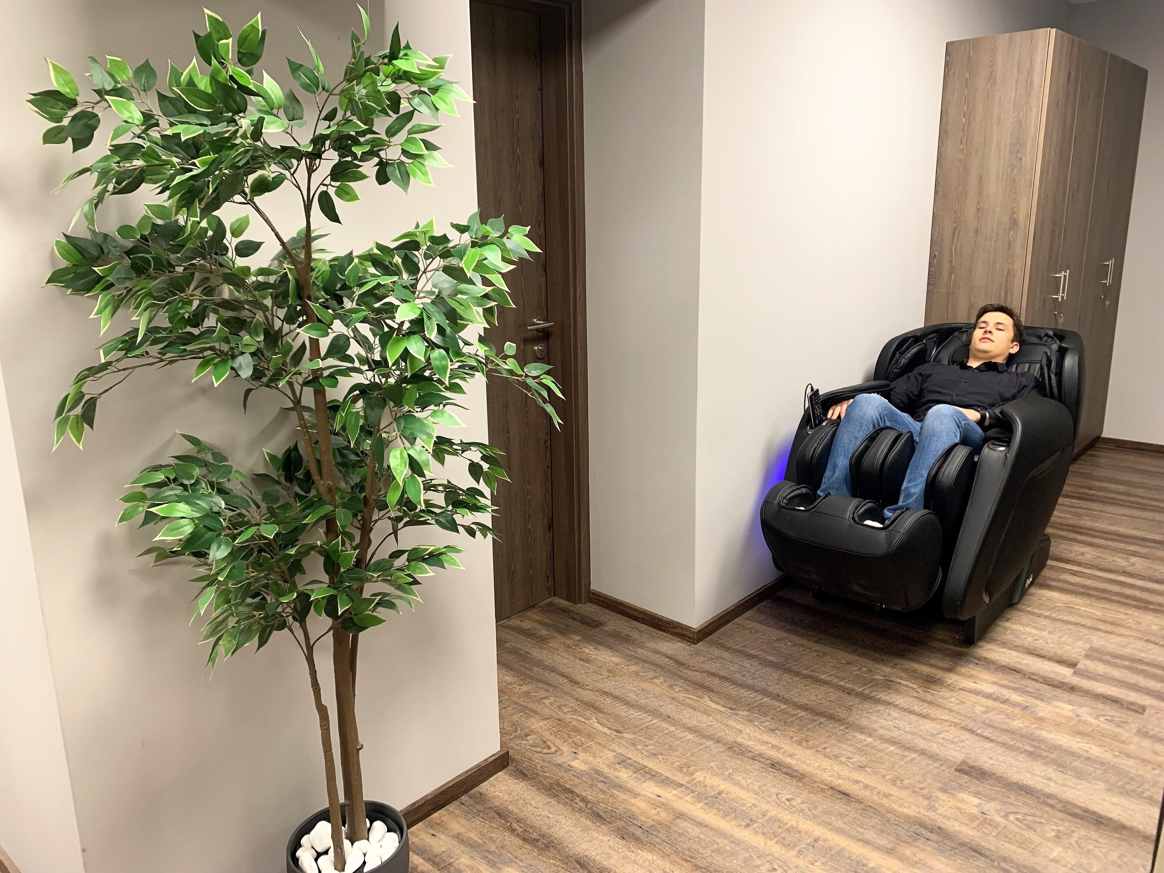 A massage chair in a room with wooden flooring and a potted plant.