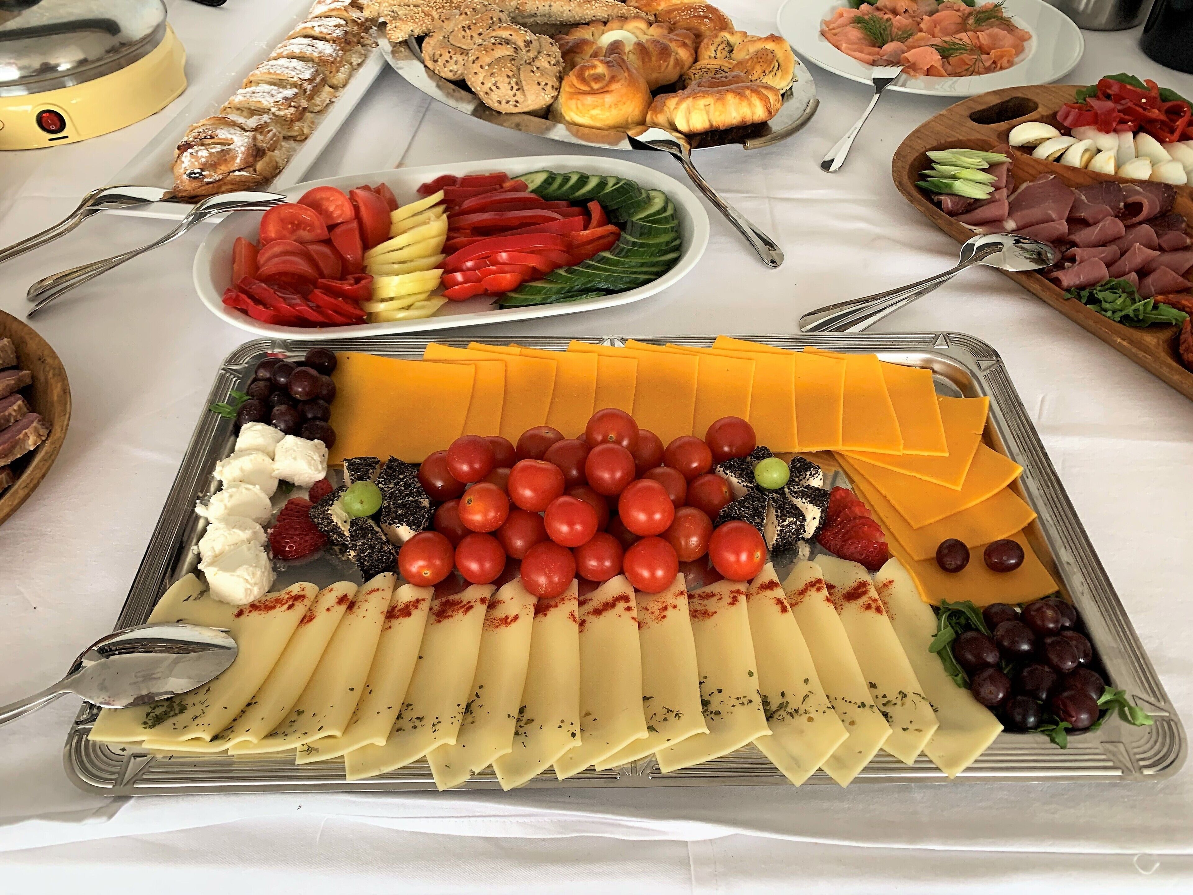 Uma mesa de buffet com diversos alimentos, incluindo queijo, tomate, azeitonas e carnes.