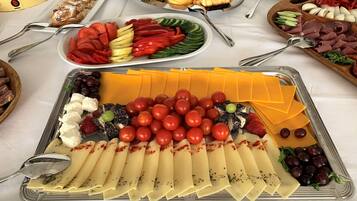 Uma mesa de buffet com diversos alimentos, incluindo queijo, tomate, azeitonas e carnes.