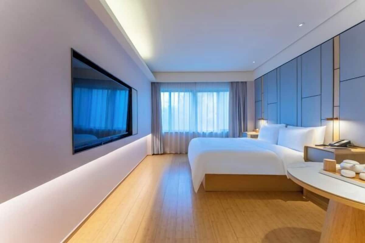 Una habitació d'hotel moderna amb un llit gran, un televisor de pantalla plana, una tauleta de nit i una finestra gran amb cortines.