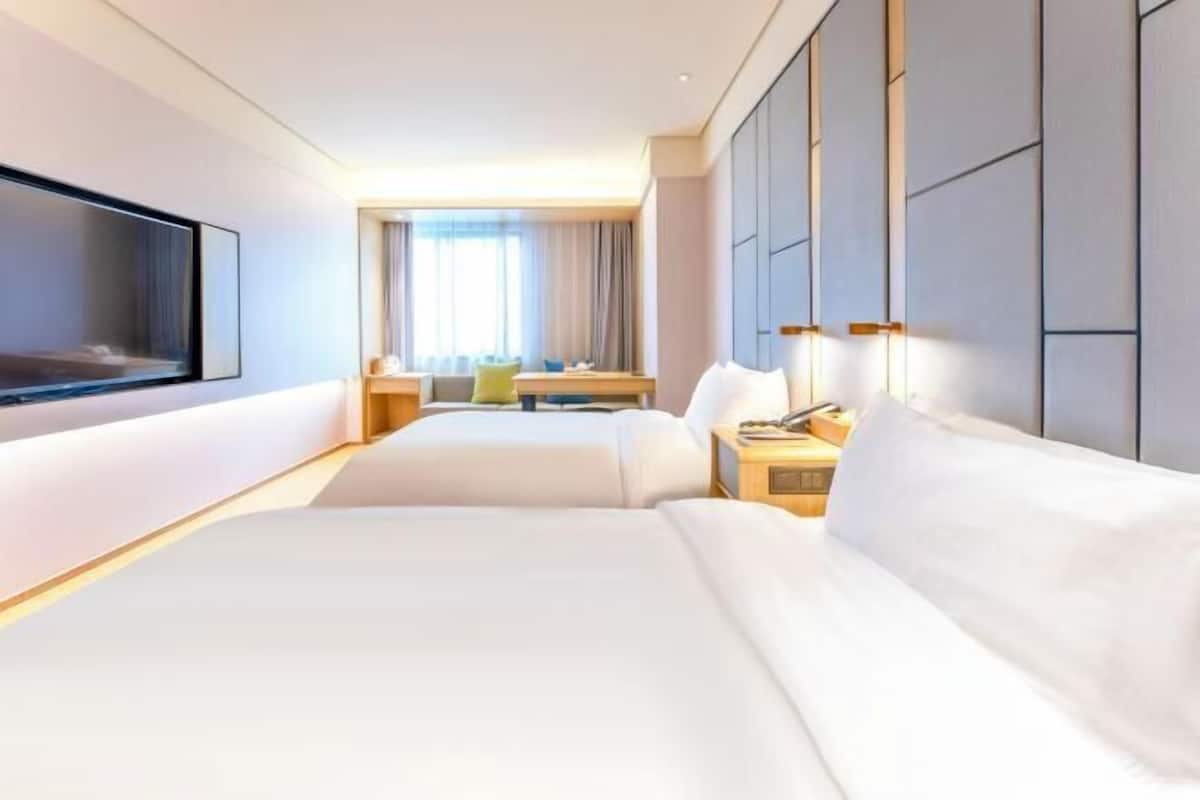 Habitació d'hotel amb un llit gran, una televisió penjada a la paret, un escriptori amb una cadira i una finestra amb cortines.