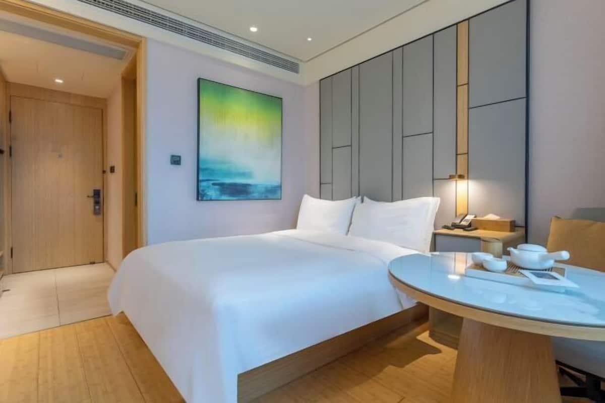 Habitació d'hotel amb un llit, una taula rodona amb una tetera, un quadre a la paret i una porta de fusta.