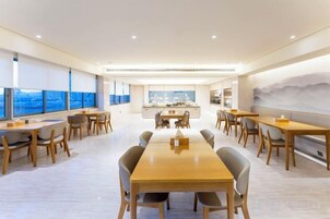 Un comedor moderno con una larga mesa de madera y sillas, una zona de cocina al fondo y ventanas grandes con vistas.