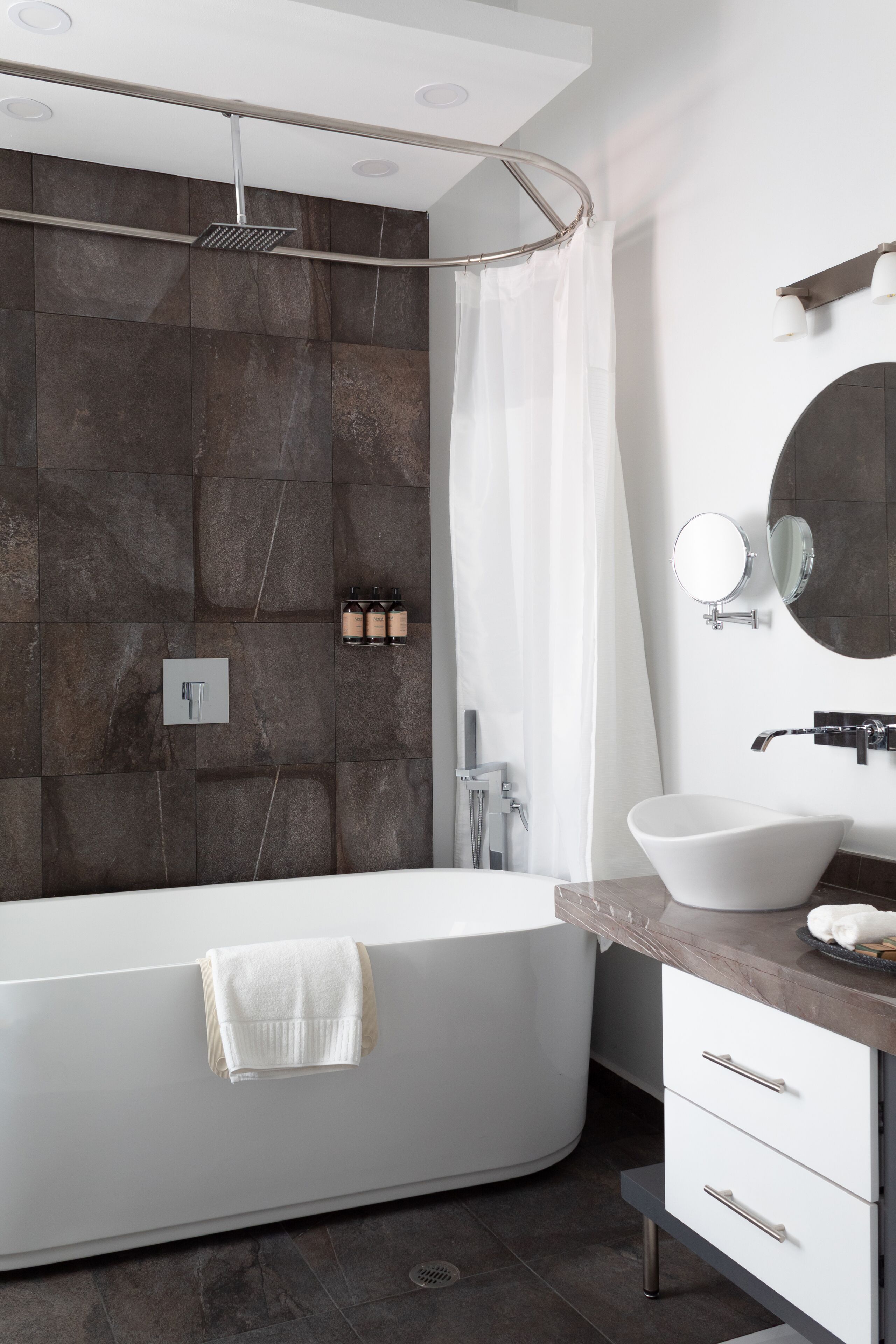 Une salle de bain moderne avec une baignoire sur pieds, un grand miroir et un lavabo fixé au mur.
