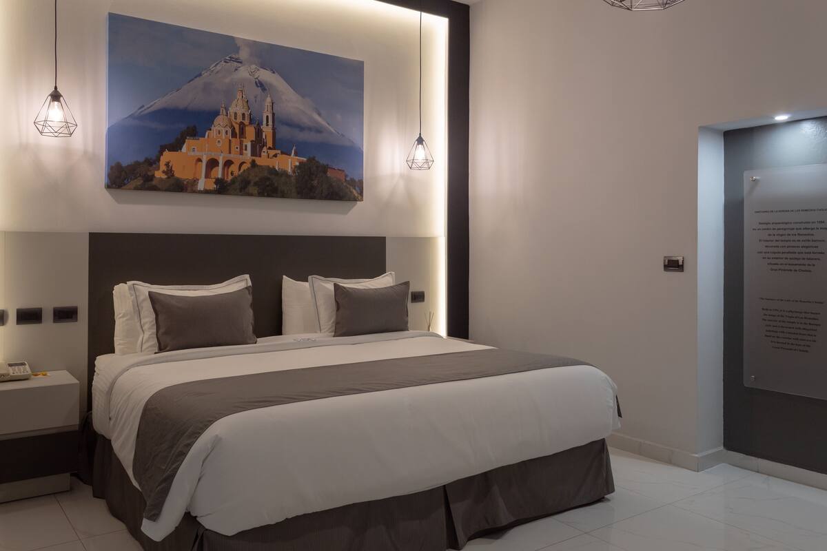 Ein modernes Schlafzimmer mit einem großen Bett, zwei Nachttischlampen, einem Nachttisch und einem Wandbild von Berg und Kirche.