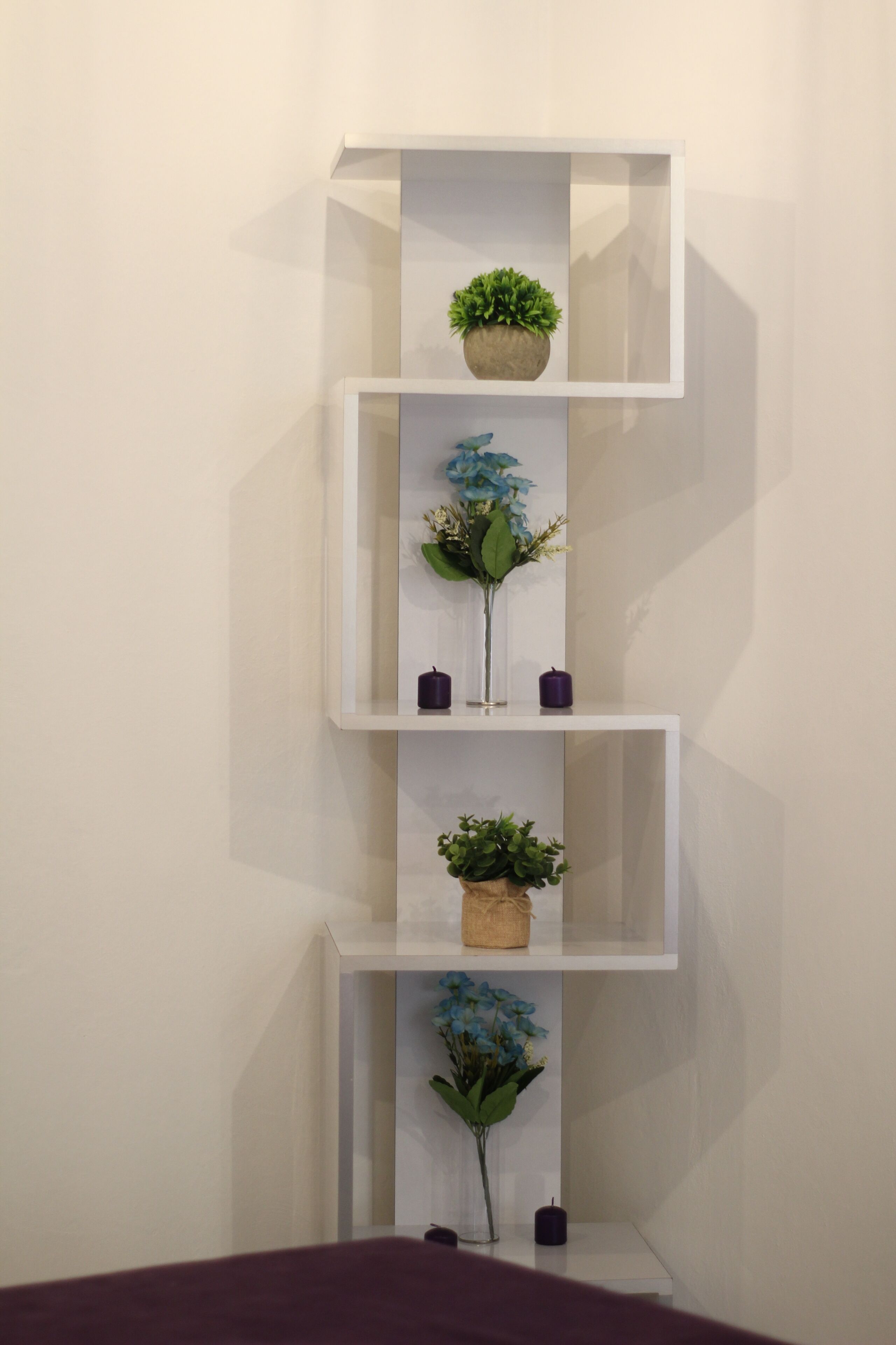 A white shelving unit with three shelves, each holding a potted plant and a candle.