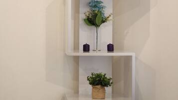 A white shelving unit with three shelves, each holding a potted plant and a candle.