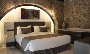 A modern bedroom with a stone arch, a bed with white and grey bedding, a nightstand with a phone, and a painting above the bed. - Hotel Boutique Casona de Santa Clara (Puebla)