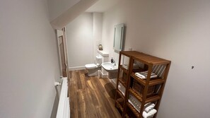 A compact bathroom with a toilet, bidet, and a wooden shelf unit with baskets. - NEW 1BD Contemporary Home Upper Dunblane (Dunblane)