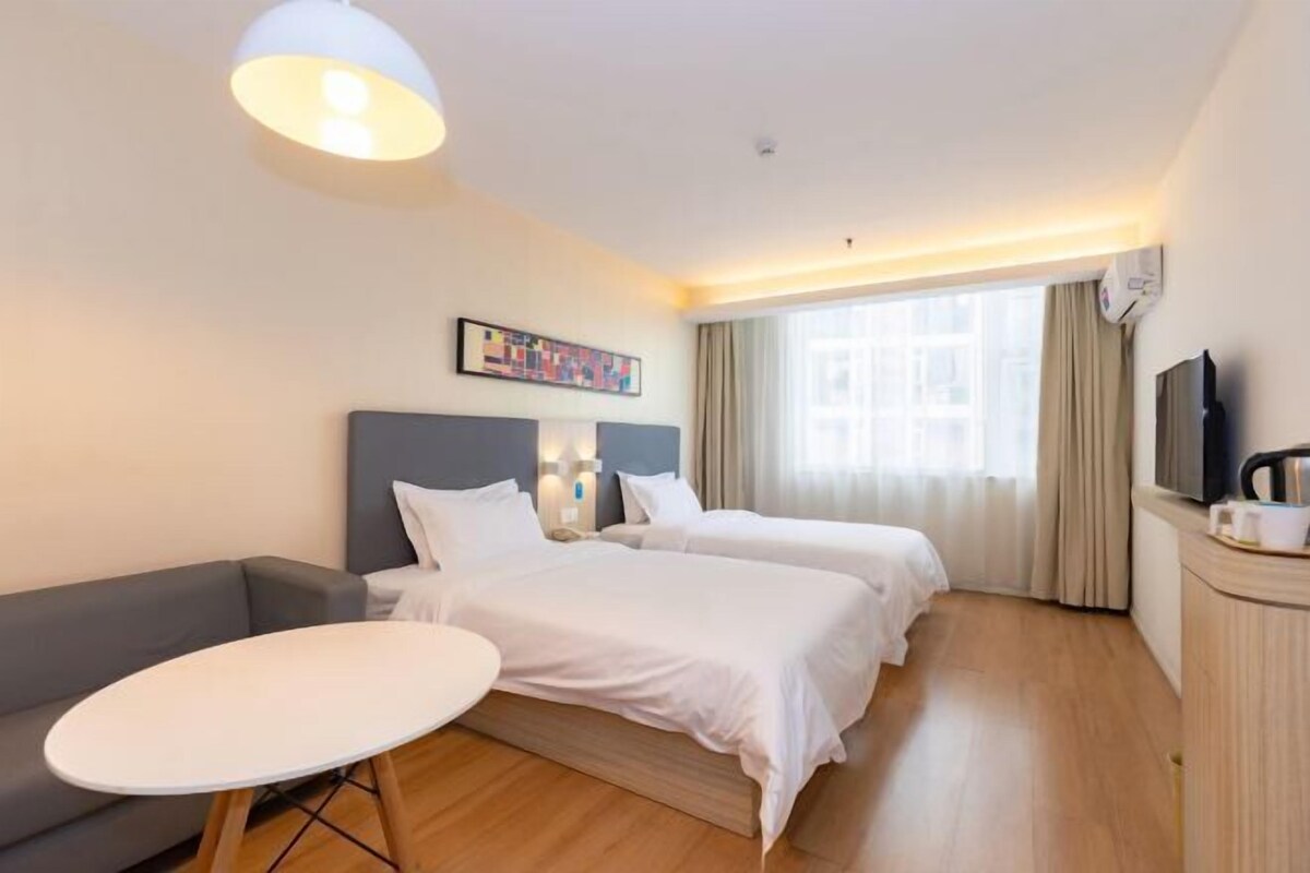 A hotel room with two beds, a sofa, a small round table, a TV, and a painting on the wall.