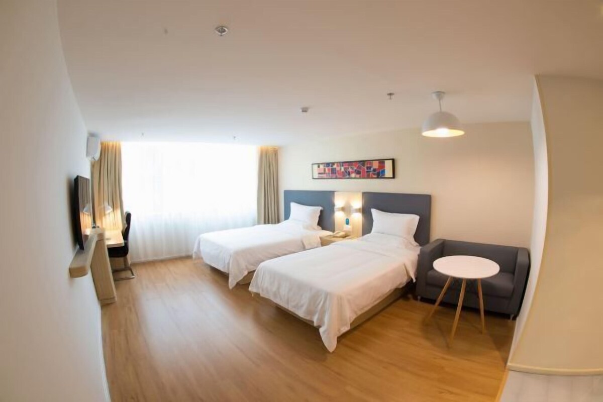 A hotel room with two beds, a desk, a chair, a sofa, and a small table.