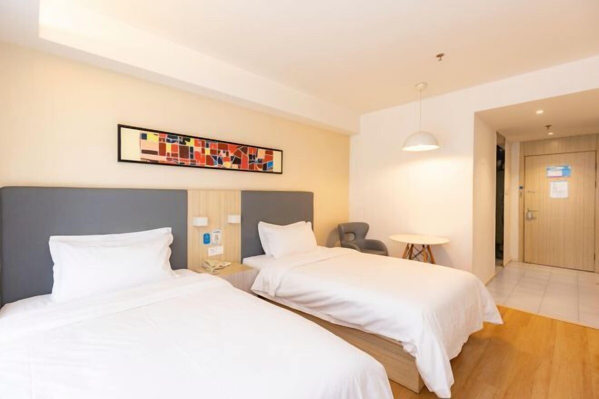 A hotel room with two beds, a small table, a chair, and a painting on the wall.