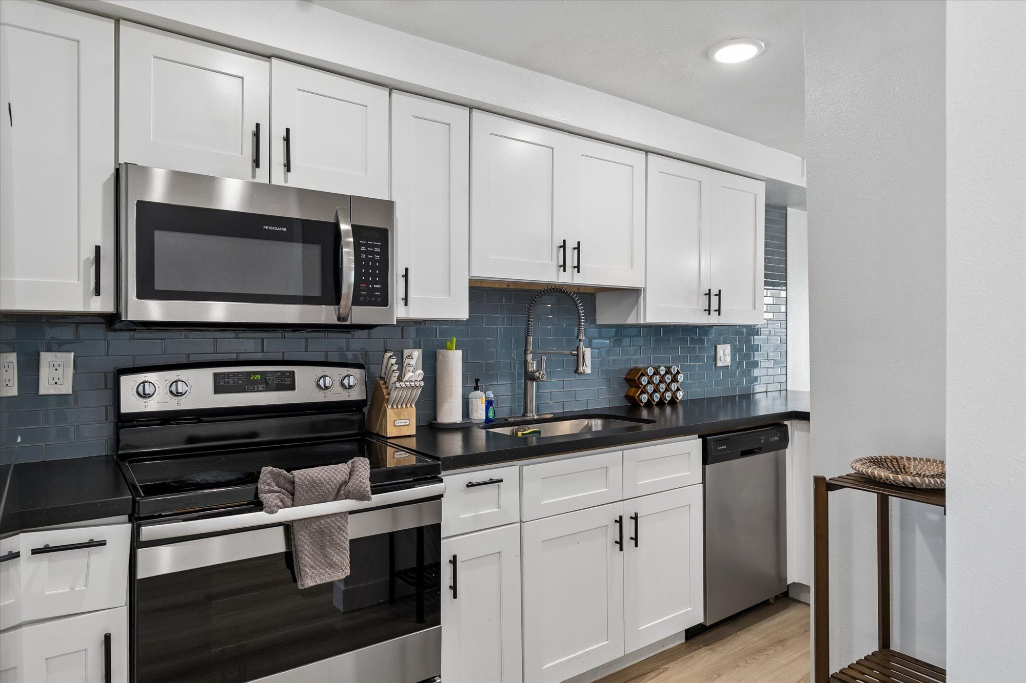 A modern kitchen with white cabinets, a stainless steel microwave, a gas stove, and a dishwasher.
