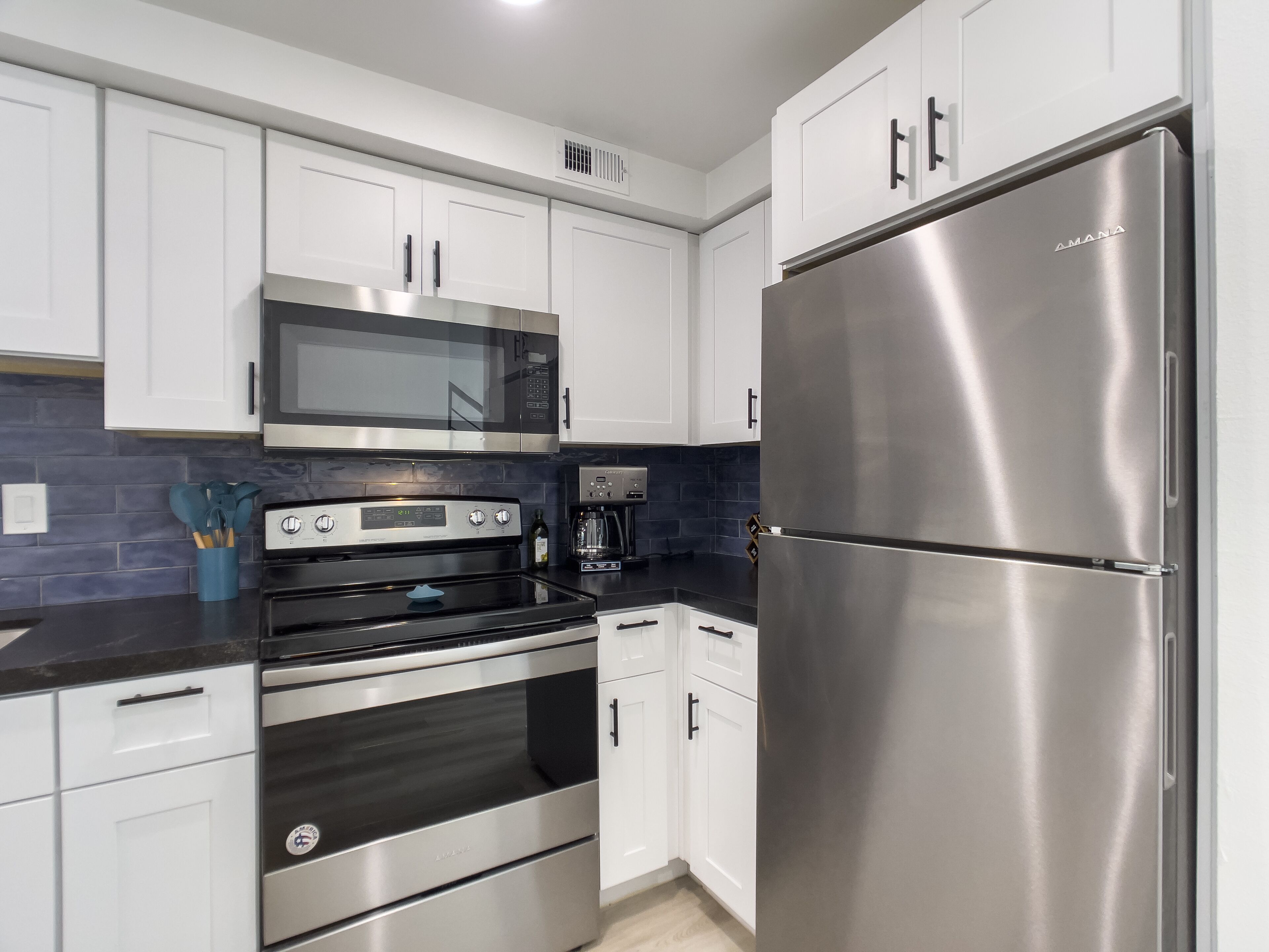 A modern kitchen with stainless steel appliances, white cabinetry, and a blue-tiled backsplash.