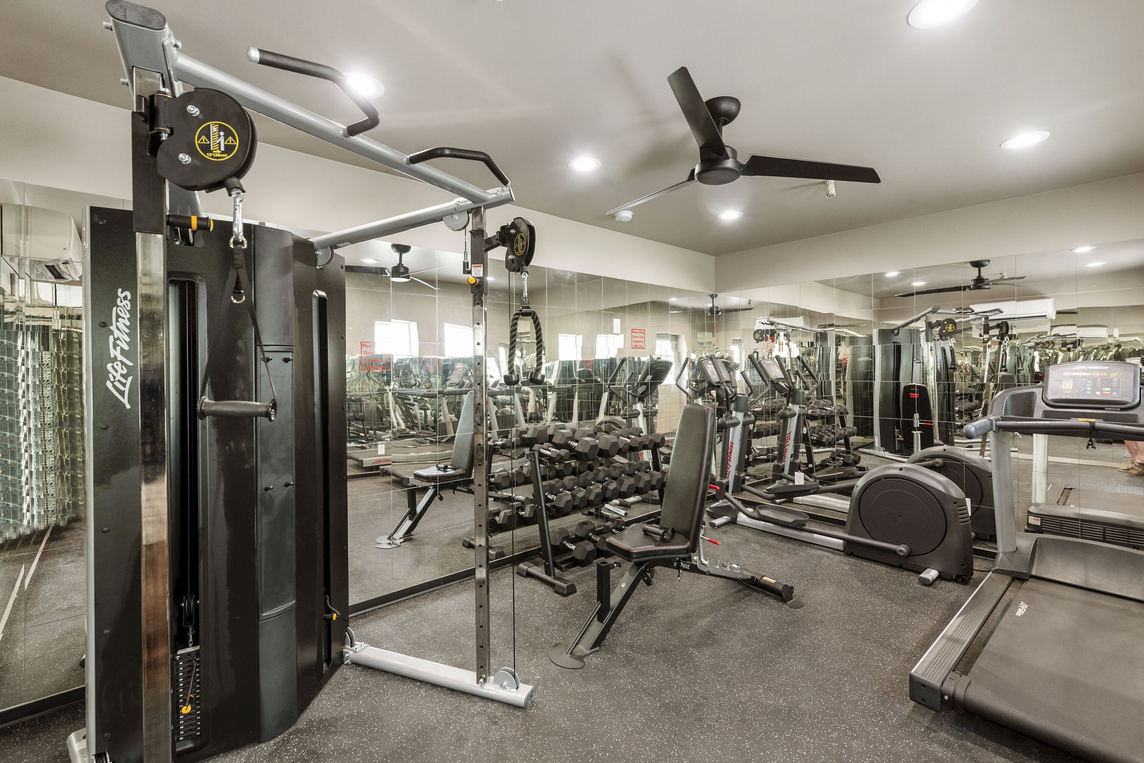 Ett gym med olika typer av träningsutrustning, inklusive en kabelmaskin, hantlar, löpband och en bänkpress.