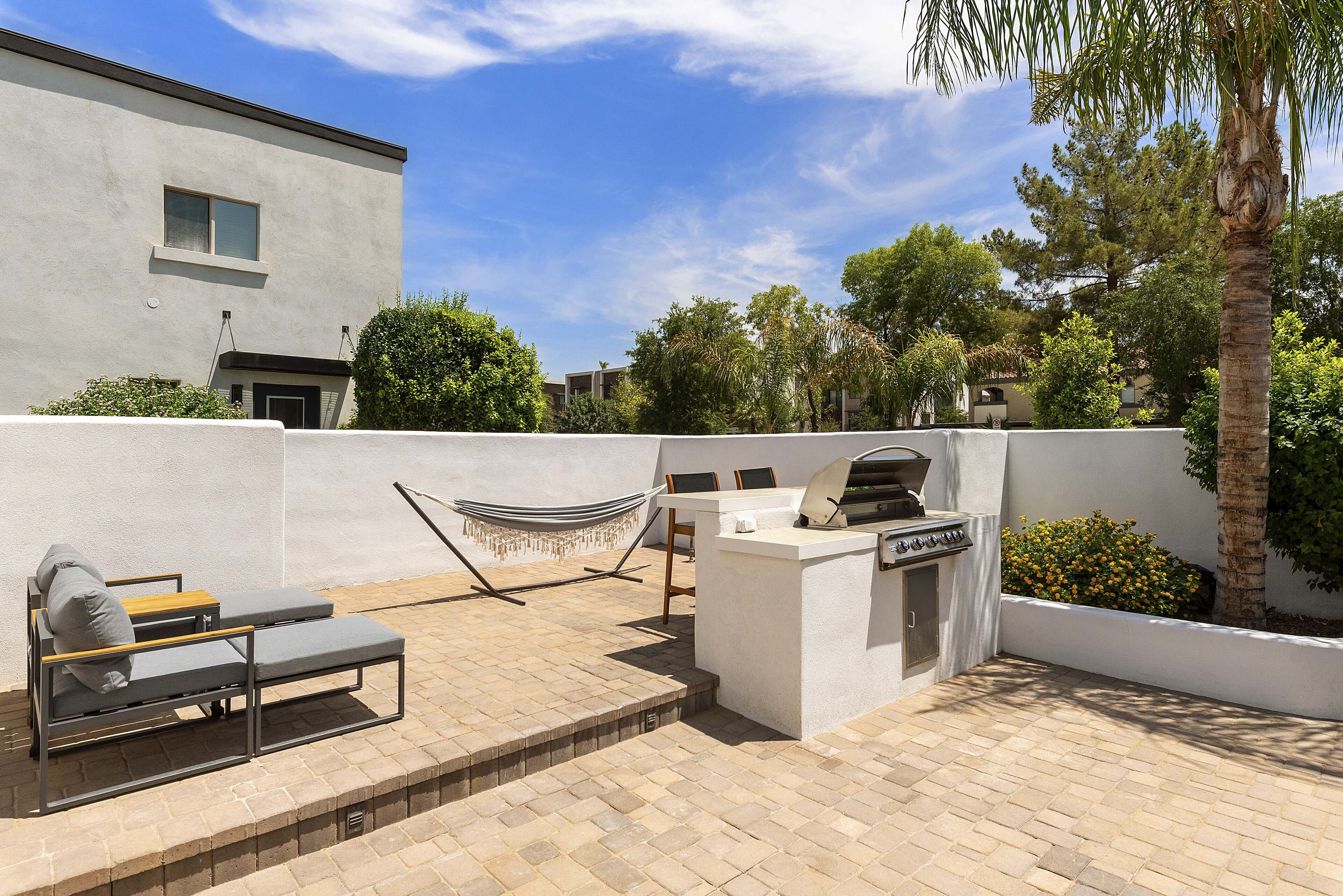 An outdoor patio with a grill, seating, and a hammock.