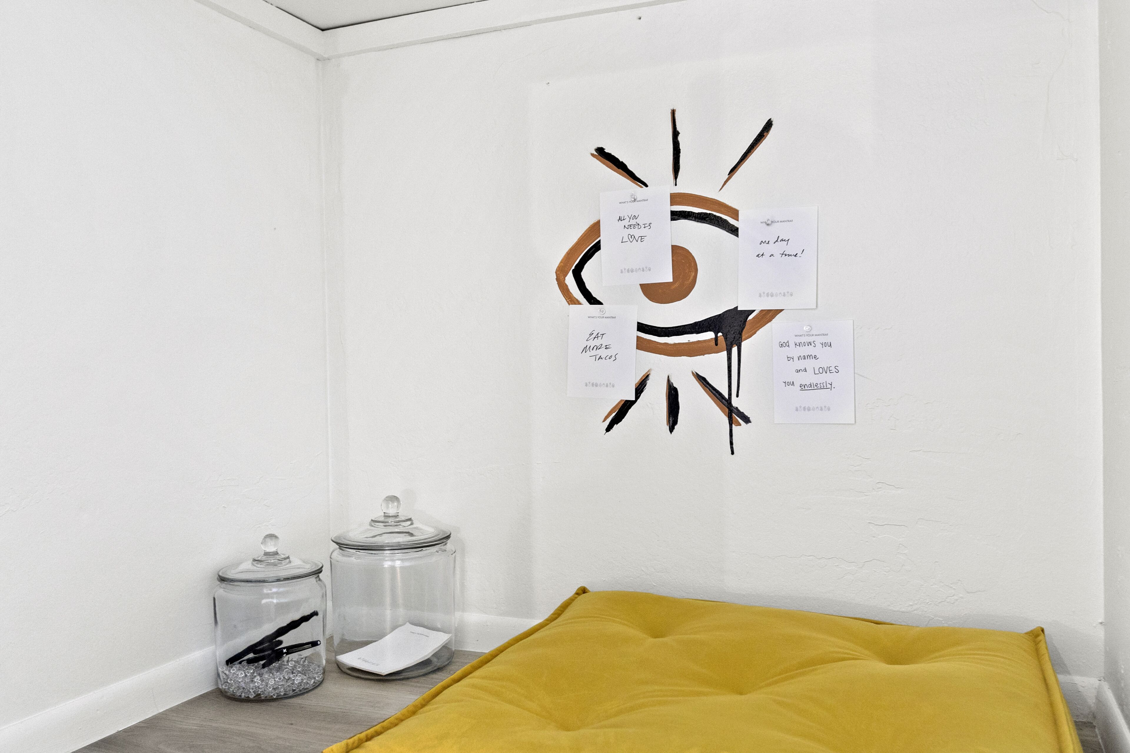 A corner of a room with a white wall, a yellow cushion, and two glass jars with lids.