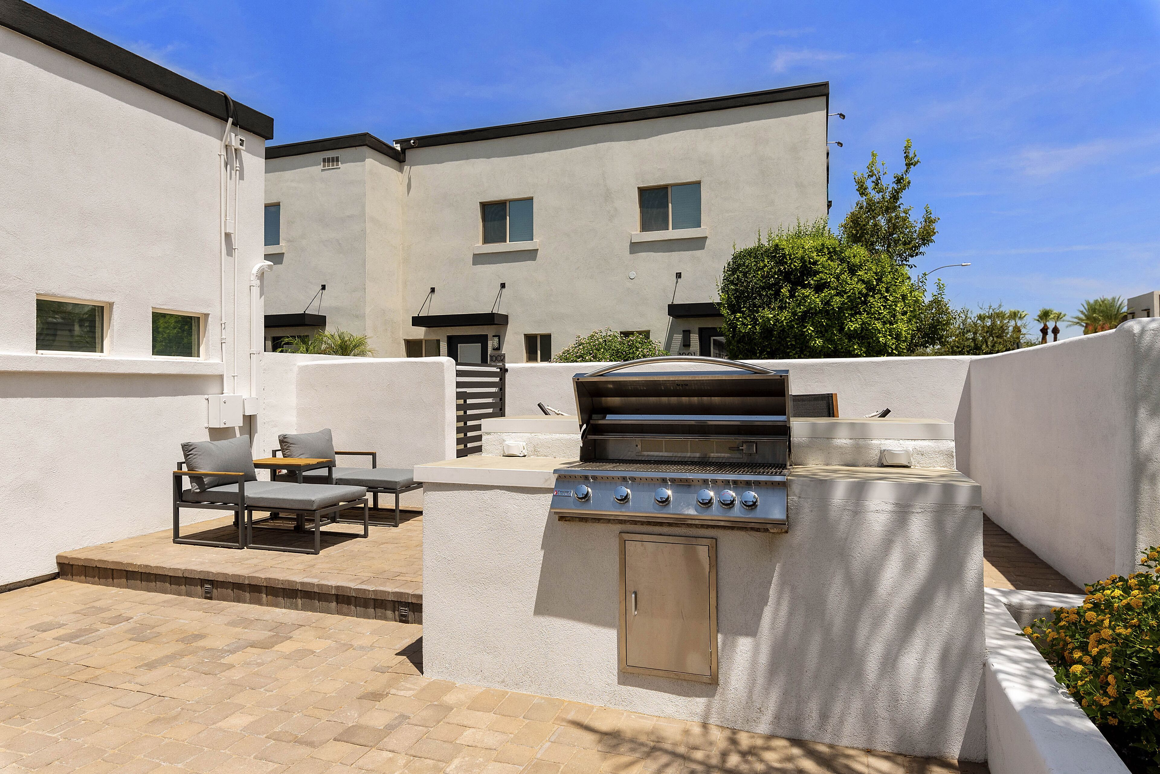An outdoor patio with a built-in grill, seating area, and a view of a modern building in the background.