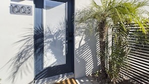 A modern building with a black door, a number '1003' sign, and a palm tree in the foreground. - Sophia (Scottsdale)