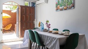 Et spiseområde med et bord dækket til to personer, grønne stole, et hvidt borddække og et billede af kaktusser på væggen.