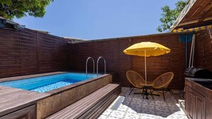 En baghave med swimmingpool, træterrasse, udendørs møbler og grill.