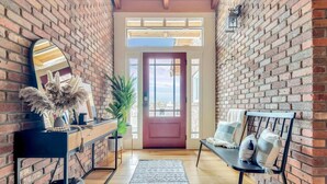 A narrow hallway with brick walls, a wooden floor, a black console table with decorative items, a bench with cushions, and a red door at the end. - 15 Acre Luxury Estate | VIP Experience (Paso Robles)