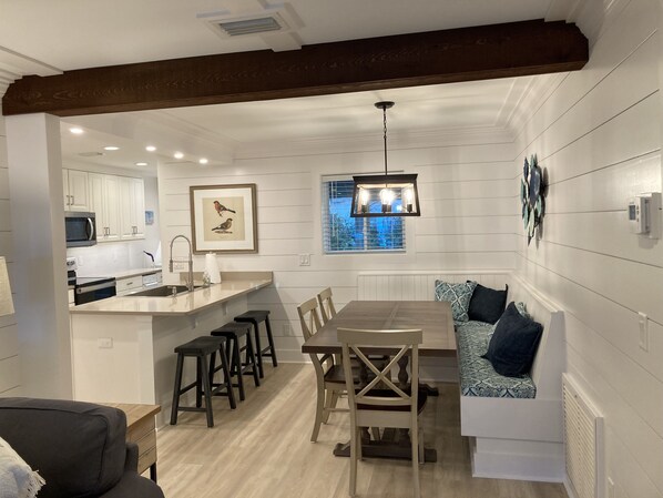 A modern kitchen with white cabinets, a central island with stools, and a dining area with a wooden table and chairs.