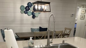 Ett modernt kök med en diskho i rostfritt stål, vita skåp och en dekorativ lampa ovanför bänkskivan.