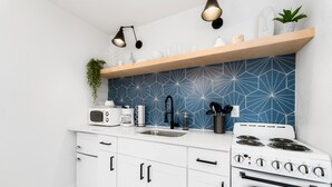 Cozinha moderna com armários brancos, fogão, pia e painel de fundo geométrico azul.
