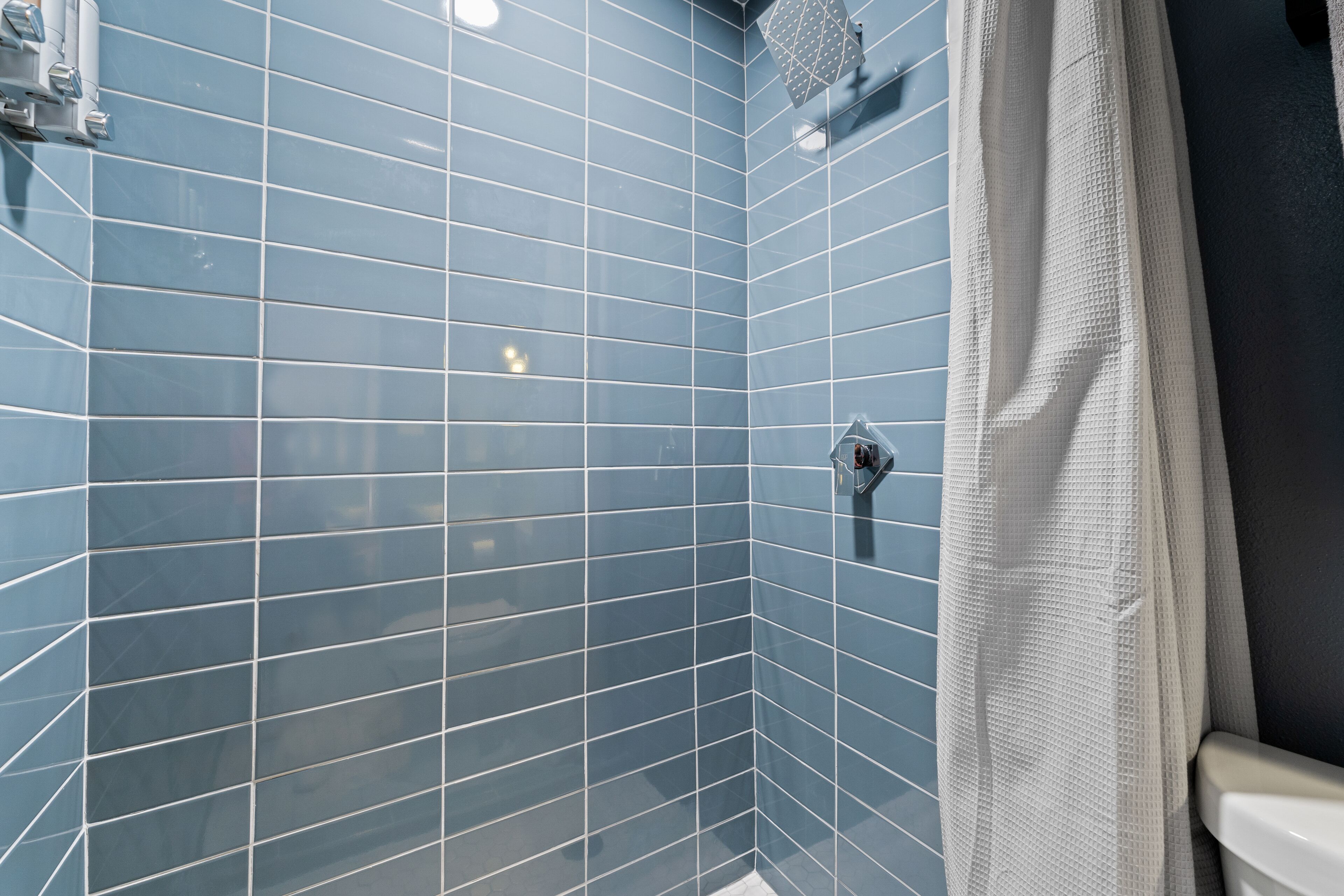 Une salle de bain avec des murs recouverts de carreaux bleus, un espace douche et un rideau blanc.