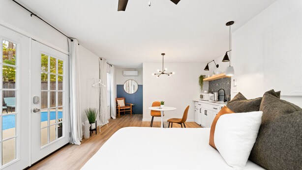 Quarto de hotel moderno com uma cama grande, área de refeições e vista para uma piscina.
