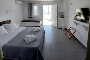 A bedroom with a bed, a TV, a balcony, and a view of the sea. - Ambience Suites (Santorini)
