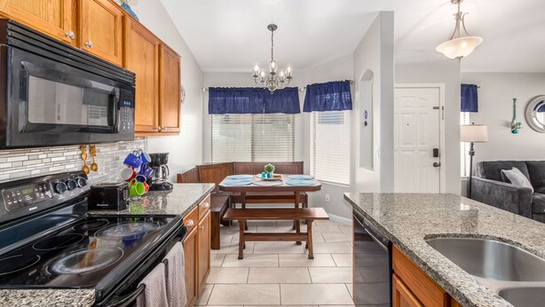 A kitchen with wooden cabinets, a black microwave, a stove, and a dining area with a table and chairs.