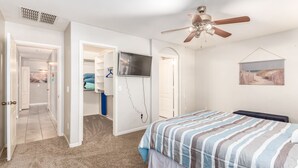 A bedroom with a bed, a ceiling fan, a TV, and a door leading to a closet.