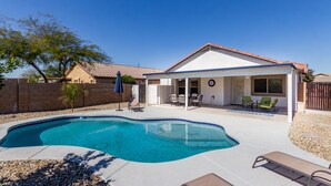 A backyard with a swimming pool, patio furniture, and a covered seating area.