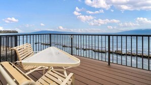 Eine Holzterrasse mit Tisch und Stühlen mit Blick auf ein Gewässer, eine felsige Küste und eine ferne Bergkette.