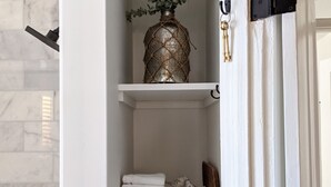 A bathroom with white marble tiles, a towel rack, a shelf with folded towels, a decorative vase, and a key on the wall. - Four Bed Family Stay. Near Sight and Sound. Hot Tub. Full Kitchen.  (Lancaster)