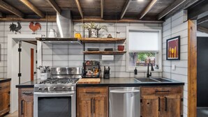 A modern kitchen with a central island, stainless steel appliances, wooden cabinetry, and a farmhouse-style ceiling. - Uniquely Modern Old Town Gem with Hot Tub (Fort Collins)