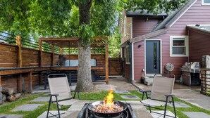 A backyard with a fire pit, two chairs, a wooden deck, and a house in the background. - Uniquely Modern Old Town Gem with Hot Tub (Fort Collins)