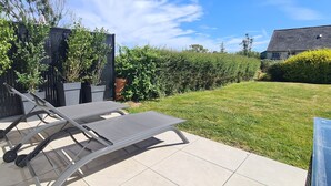 A patio with a grill, lounge chairs, and a well-maintained lawn.
