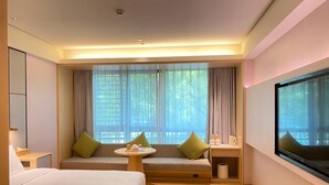 A hotel room with a bed, a seating area with cushions, a small table, a TV, and a window with curtains. - Ji Hotel (Huzhou)